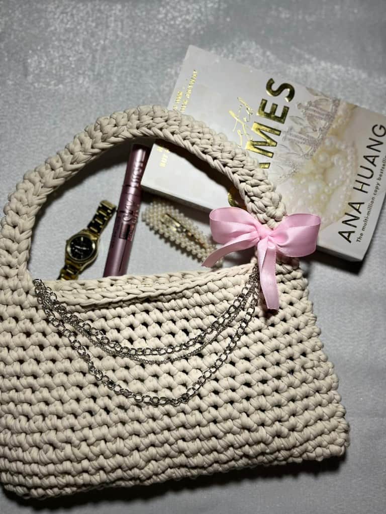 Tamborēta bēša rokassoma ar rozā lentīti un sudraba ķēdīti.